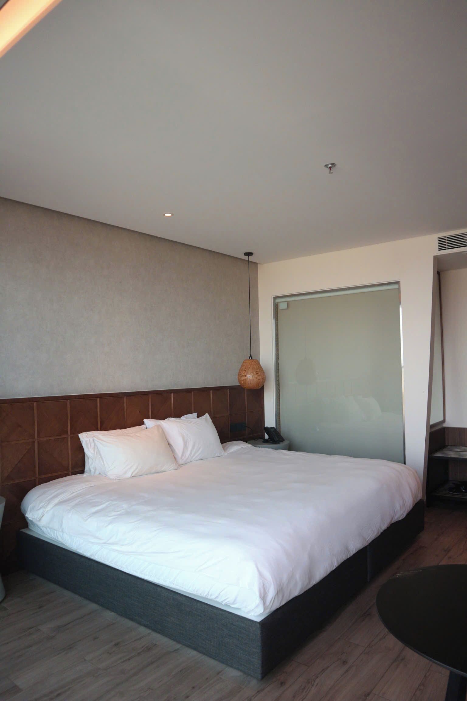 Une chambre d’hôtel moderne avec un grand lit, une table de chevet, un miroir et une petite table.