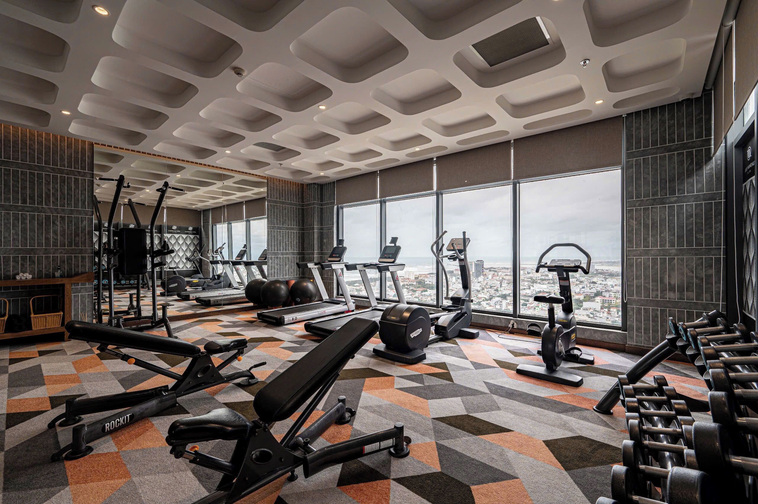 A gym with various exercise equipment, a patterned floor, and large windows offering a city view.
