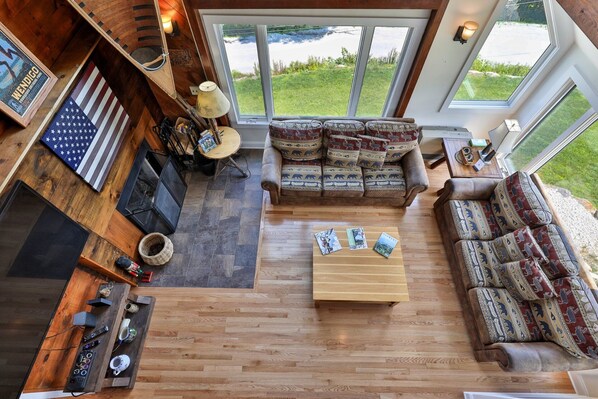 A cozy living room with a sofa, a coffee table, and a fireplace. There are windows providing a view of the outdoors.