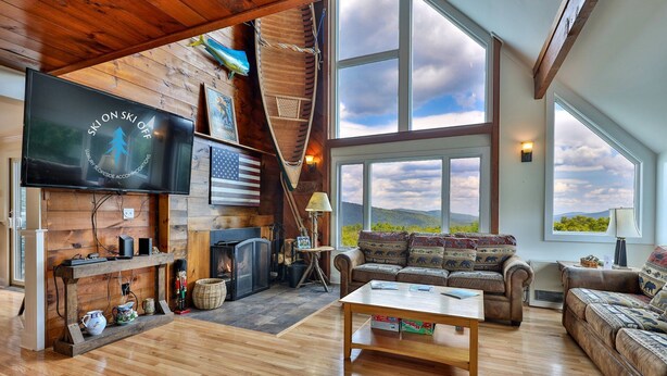 A spacious living room with a fireplace, a television, and a large window offering a mountain view.