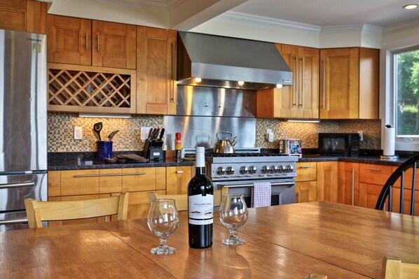 Una cocina con armarios de madera, electrodomésticos de acero inoxidable y una mesa de comedor con copas de vino y una botella.