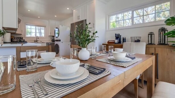 Una cocina moderna con armarios blancos, una mesa de comedor de madera para cuatro personas y un amplio ventanal que proporciona luz natural.