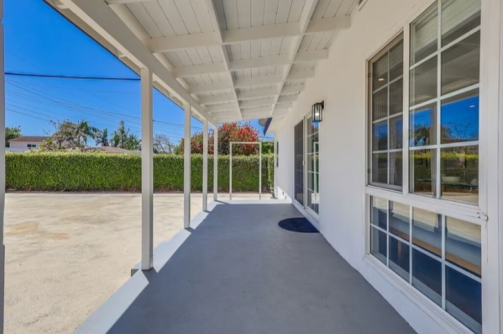 Un espacio al aire libre techado con piso de concreto, columnas blancas y ventanas grandes.
