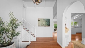 Un interior moderno con una escalera de madera, un cuadro abstracto grande y vistas hacia una zona de cocina.