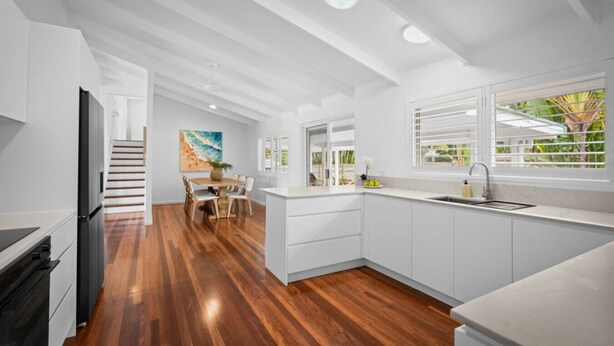 Una cocina moderna con armarios blancos, una mesa de comedor de madera y vistas a un jardín a través del ventanal.