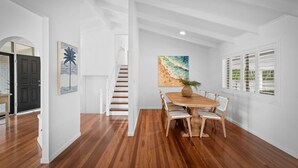 Un comedor con una mesa y sillas de madera, una escalera y un cuadro con motivos playeros en la pared.