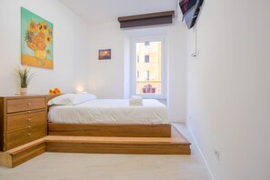 Una camera da letto con un letto, una cassettiera in legno, un quadro, una finestra e una televisione.