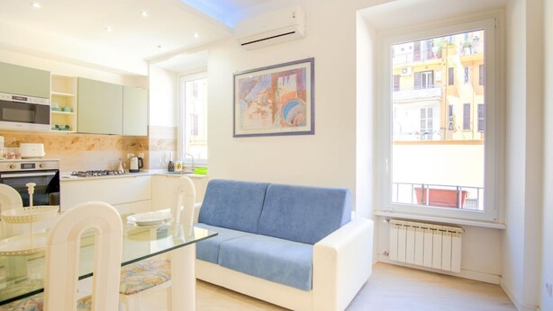 A modern apartment with a kitchen, dining area, and a living room with a sofa and a large window. - Elegantis.it Doris Suite Apartment - One Minute Walk to Vatican Museums (Roma)