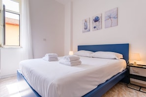 Uma cama bem arrumada com lençóis e toalhas brancos, cabeceira azul e três obras de arte penduradas na parede.