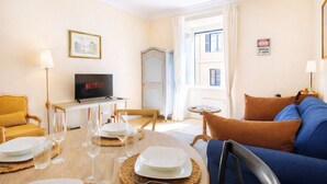 A living room with a dining table set, a sofa, a TV displaying Netflix, and a sign that says 'Genius at Work'. - Elegantis.it Milos Suite Apartment - Your Chic Retreat in Central Rome (Roma)
