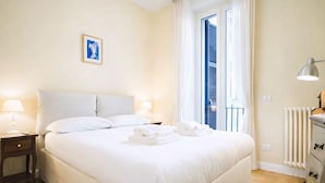 A hotel room with a large bed, two bedside lamps, a radiator, and a window with curtains. - Elegantis.it Milos Suite Apartment - Your Chic Retreat in Central Rome (Roma)