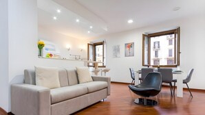 A modern living room with a sofa, a dining table with chairs, and a window with a view of buildings.