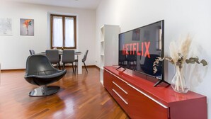 A modern living room with a flat-screen TV, a dining area, and a red entertainment unit.
