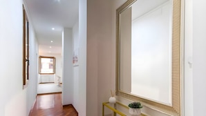 A hallway with a wooden floor, a yellow console table with a mirror, and a potted plant.