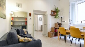 A modern living room with a sofa, dining table, chairs, and a bookshelf. - Elegantis.it Trastevere Modern Apartment Comfort in Rome Most Charming District (Roma)