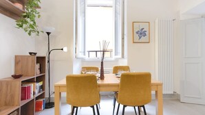 A dining area with a table, chairs, a bookshelf, a floor lamp, and a window with a view. - Elegantis.it Trastevere Modern Apartment Comfort in Rome Most Charming District (Roma)