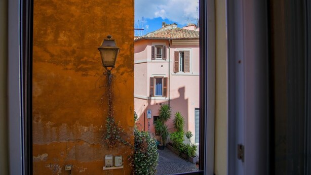 A view through a doorway of a building with a pink facade, a small courtyard, and a street visible in the background. - Elegantis.it Trastevere Modern Apartment Comfort in Rome Most Charming District (Roma)