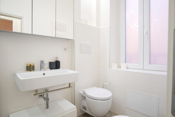 Un baño moderno con un lavabo blanco, inodoro y ventana.