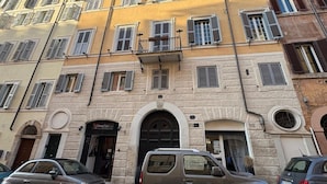 A multi-story building with a stone facade, multiple windows with shutters, and a central entrance with an arched doorway.