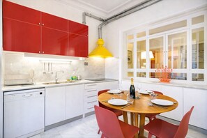 Een moderne keuken met rode kastjes, een houten eettafel en een gele hanglamp.