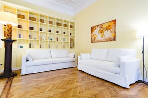 Een kamer met twee witte banken, een houten visgraatvloer, een boekenkast en een wereldkaartschilderij.