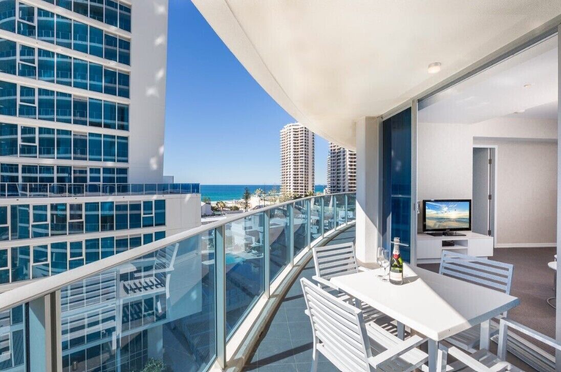 A balcony with a glass railing overlooking a beach and high-rise buildings.