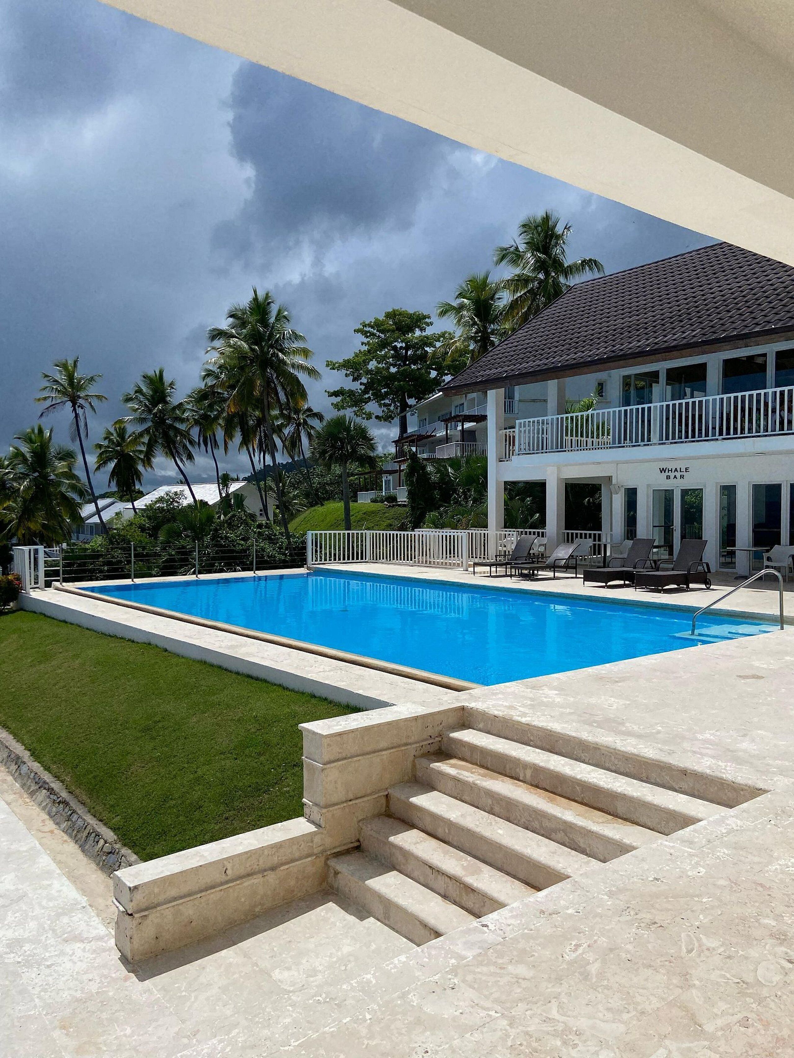 Ein zweistöckiges Gebäude mit Pool, Palmen und einem stürmischen Himmel.