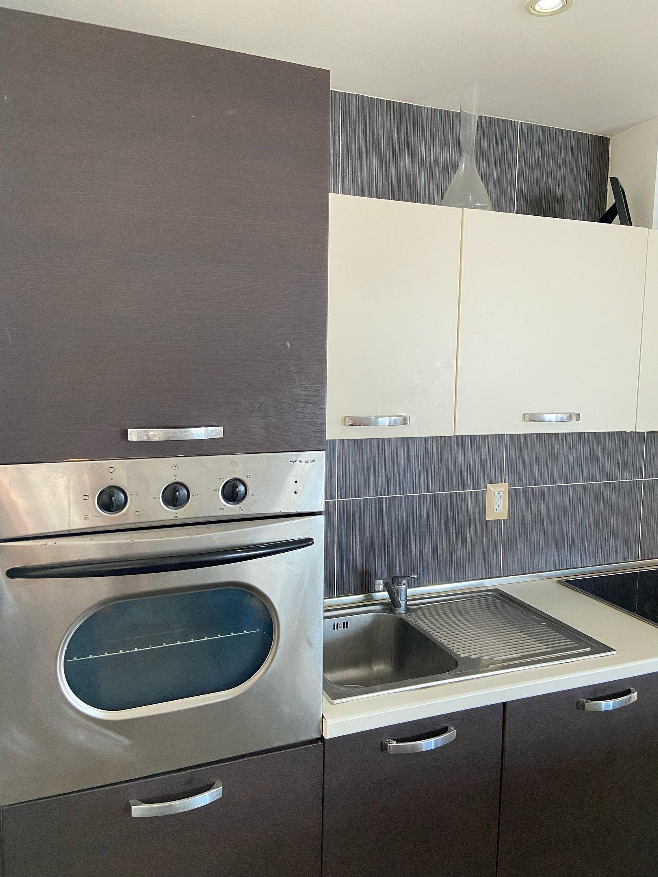 Una cocina moderna con horno empotrado, pileta de acero inoxidable y muebles oscuros.