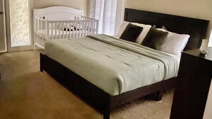 Un dormitorio con cama, cuna, ventilador de techo y ventana con cortinas.