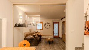 Un salon moderne avec une table à manger en bois, un canapé et une table basse. Il y a une horloge au mur et une porte qui donne sur une autre pièce.