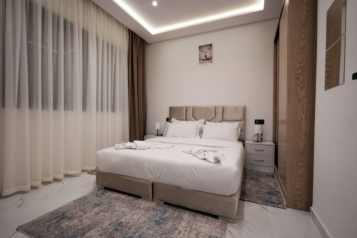 Un dormitorio moderno con una cama grande, mesitas de noche, un armario y una lámpara en el techo.