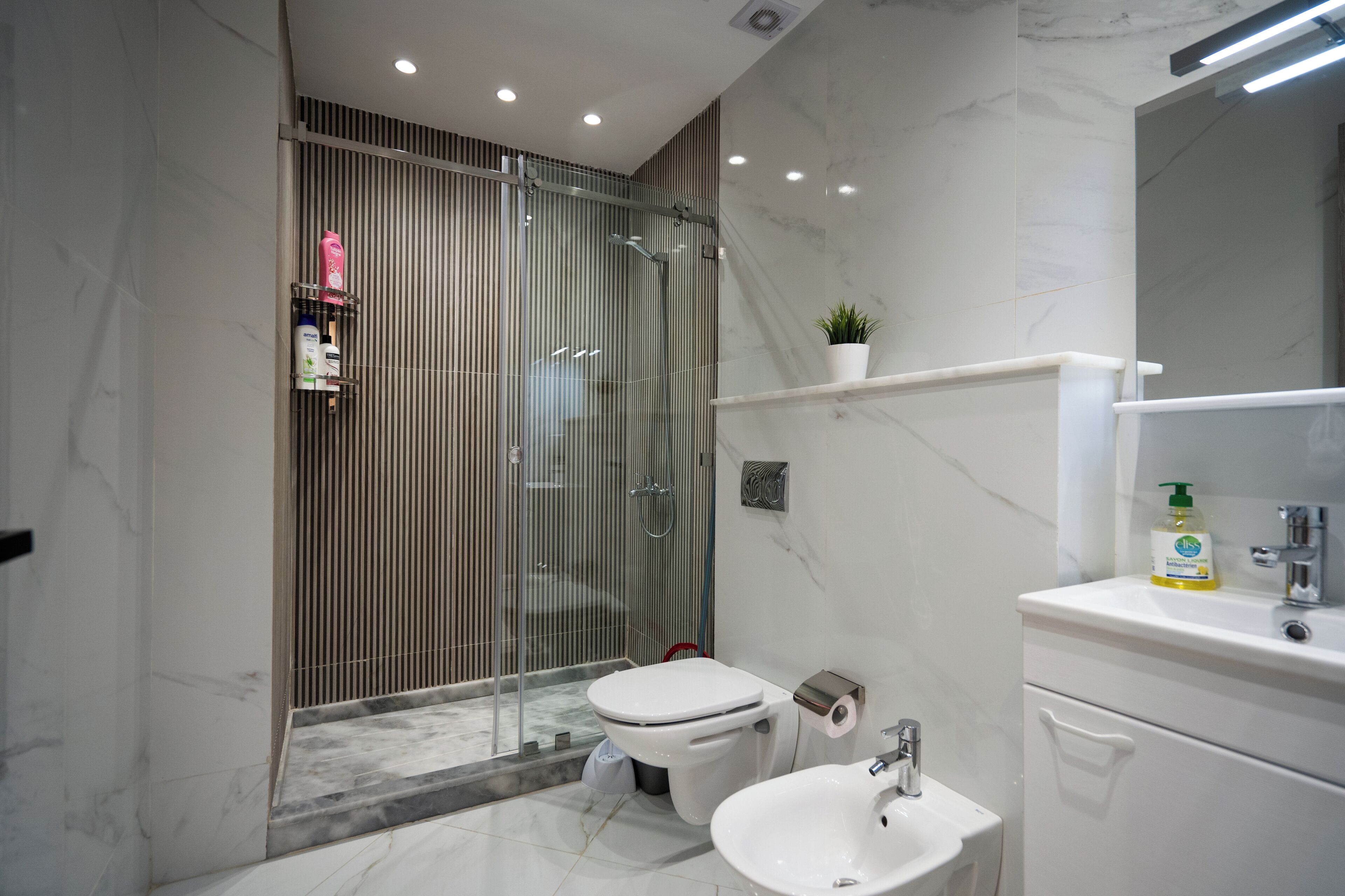 Un baño moderno con cabina de ducha de vidrio, inodoro blanco, lavamanos y espejo sobre el lavamanos.