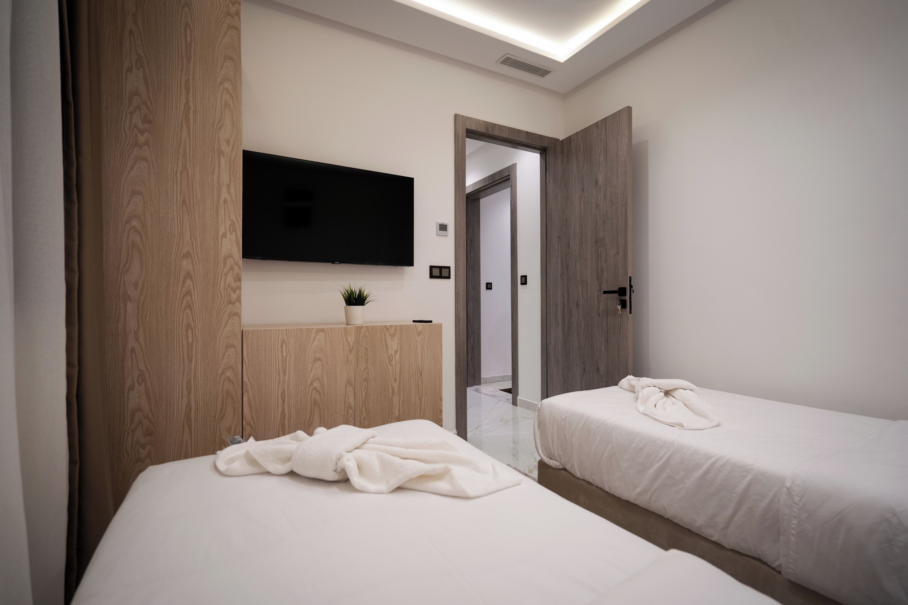 A modern hotel room with two beds, a flat-screen TV mounted on the wall, and a wooden wardrobe.