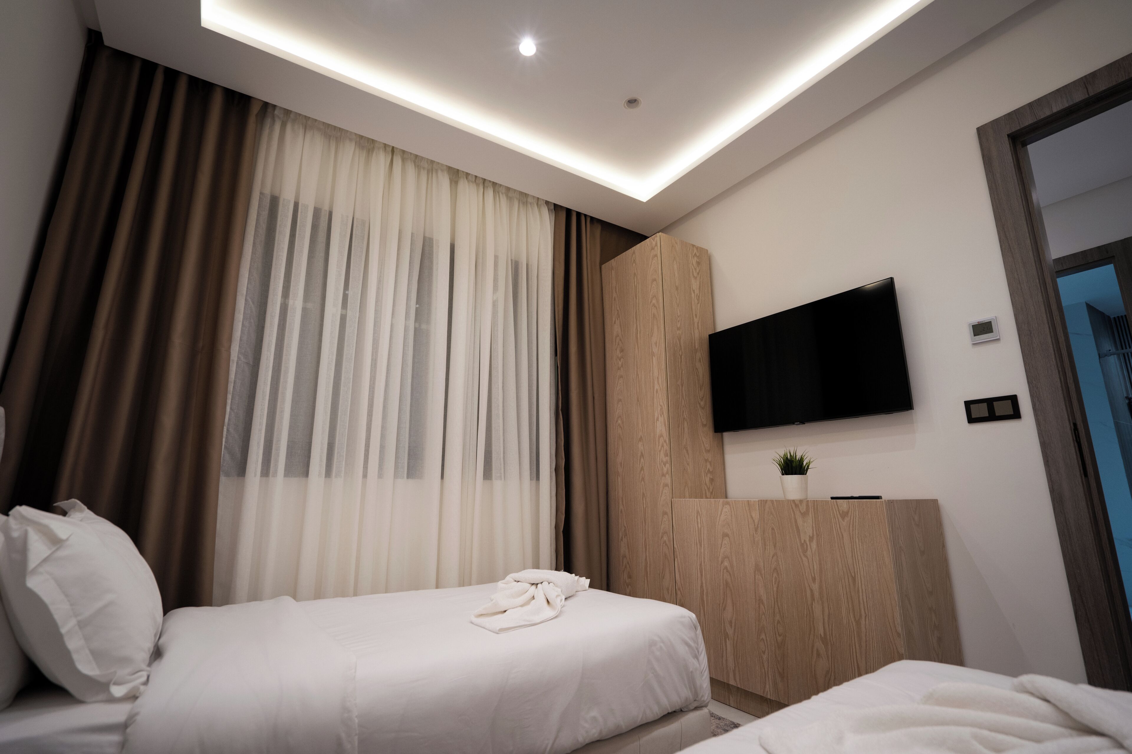 A modern hotel room with a bed, a flat-screen TV mounted on the wall, and a wooden cabinet.