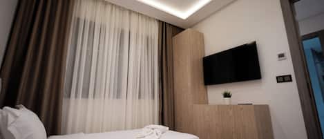 A modern hotel room with a bed, a flat-screen TV mounted on the wall, and a wooden cabinet.