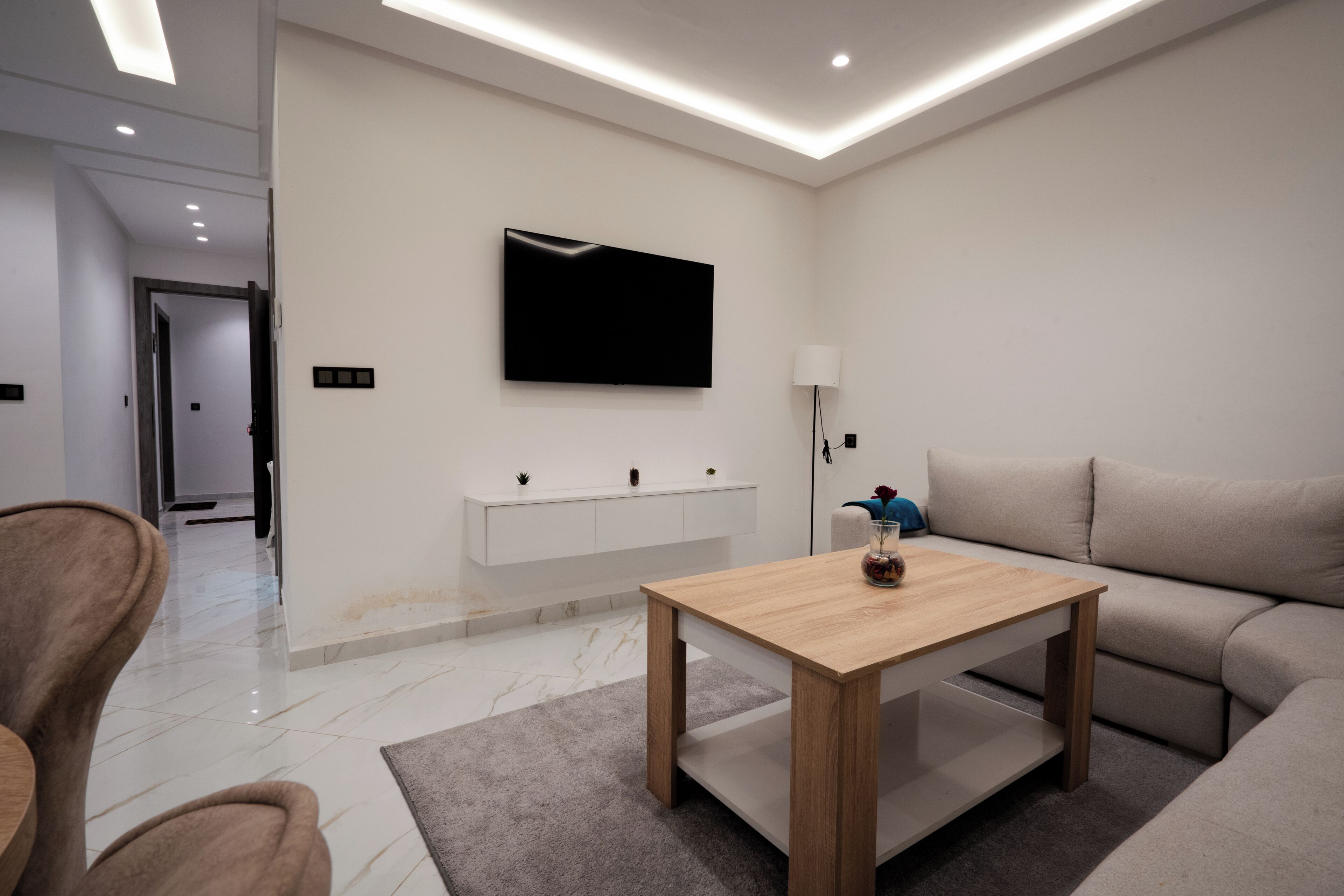 Een moderne woonkamer met een flatscreen televisie, een houten salontafel, een bank en een lamp.