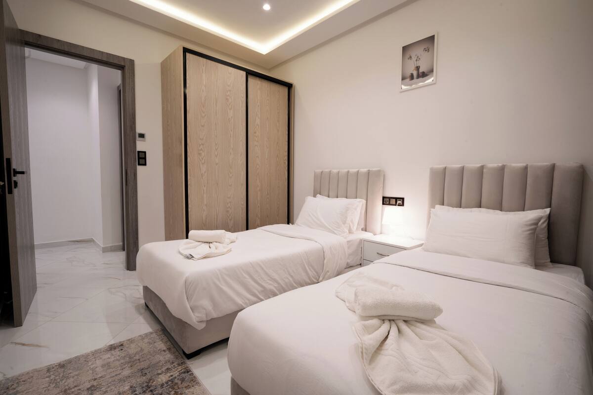Habitación de hotel con dos camas, un armario, una mesita de noche y un pequeño cuadro en la pared.