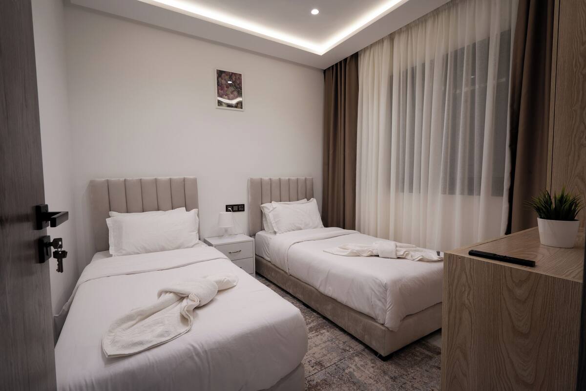 Una habitación de hotel con dos camas, una mesita de noche, una planta en maceta y una ventana con cortinas.