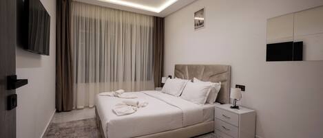 Une chambre moderne avec un grand lit, des tables de chevet, un téléviseur à écran plat et un luminaire au plafond.
