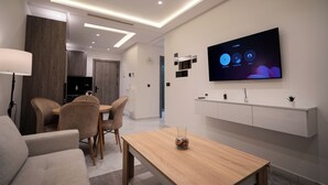 A modern living room with a wooden dining table, beige sofas, and a flat-screen TV mounted on the wall. - Living Appart Hotel (Tangier)