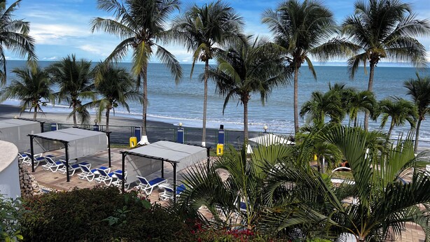 A beachside view with palm trees, a pool area with lounge chairs, and a view of the ocean. - Oceanfront in Coronado Bay (Las Lajas)