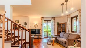 A spacious living room with a wooden staircase, a flat-screen TV, a sofa, and a coffee table.