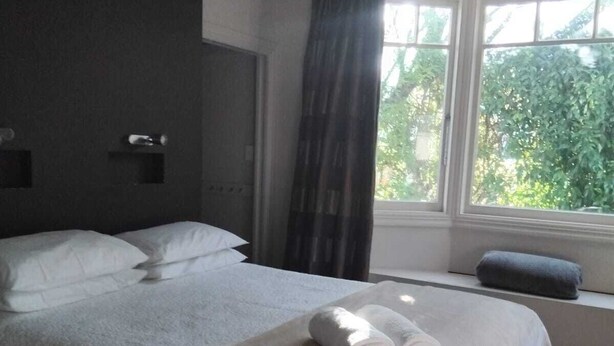 A hotel room with a large bed, a window with curtains, and a view of greenery outside. - Charming 3-bedroom house walking distance to the wonderful Napier, marine parade (Napier)