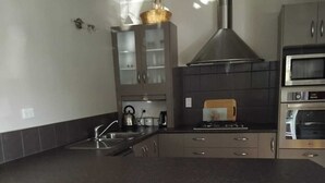 A modern kitchen with a large island, bar stools, a built-in oven, and a stainless steel range hood. - Charming 3-bedroom house walking distance to the wonderful Napier, marine parade (Napier)