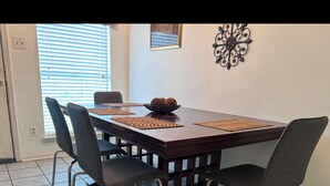 A dining area with a rectangular table, four chairs, and a decorative wall piece.