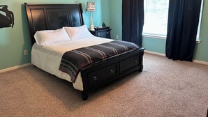 A bedroom with a bed, a nightstand, a lamp, and a window with curtains.
