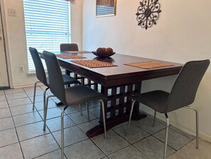 A dining area with a rectangular table, four chairs, and a decorative wall piece.