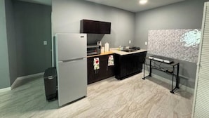 A compact kitchen with a refrigerator, dark cabinets, a countertop, and a backsplash.