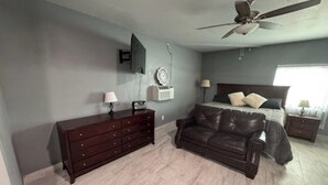 A bedroom with a bed, a dresser, a leather couch, a ceiling fan, and a wall-mounted TV.