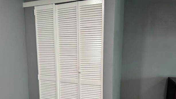 A closed white closet with horizontal louvered doors in a room with light gray walls and a tiled floor.